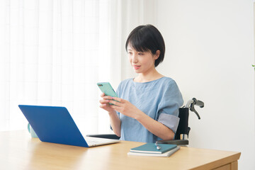 家でスマホを使う車椅子に乗った障がい者女性