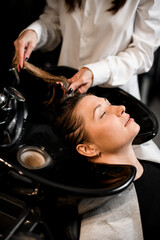 woman on hair washing chair with her eyes closed and hands of hairdresser washing her hair.