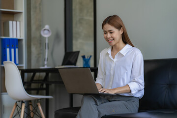 Young Asian woman sitting with laptop on black sofa meeting online in home office