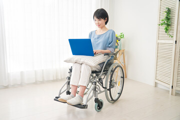 家でパソコンを使う車椅子に乗った障がい者女性