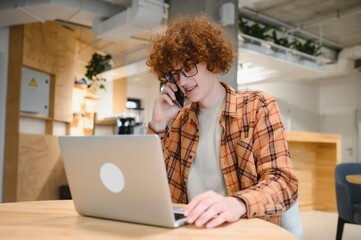Obraz premium Cheerful male freelancer making telephone call share good news about project working in cafe interior,happy hipster guy having smartphone conversation while studying in good mood writing in planner