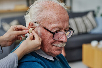 Close-up of caregiver wearing hearing aid into the ear of senior man who having hearing problems