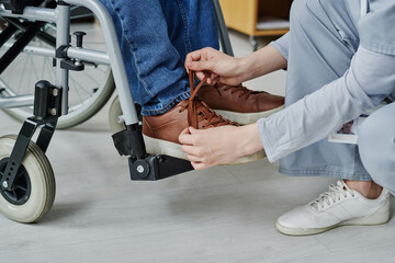 Close-up of young woman helping man with disability to tie shoelaces while he sitting in wheelchair