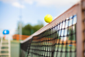 Bright greenish yellow tennis ball hitting the net.