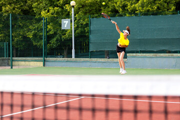Professional equipped female tennis player beating hard the tennis ball with racquet.