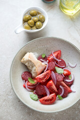Tomato salad with fried chorizo sausage and red onion, vertical shot on a beige stone background, elevated view