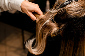 Close-up of hairdo making process. Hairdresser accurate puts female hair with comb