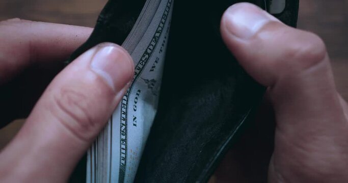 Close-up of a man opening a wallet filled with US 100 dollar bills and counting the money. Male hands count money cash in the wallet, extreme close up. Concept of money and wealth