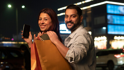 couple shopping at night and showing blank screen of smartphone
