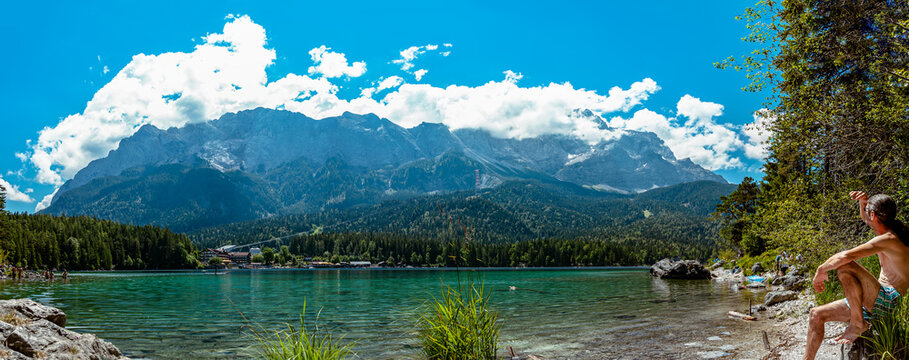 Man at Lake in the mountains in summer. Beautiful Landscape scenery. Bavarian panorama of the beach of lake Eibsee, Bavaria Germany. Mountain range of the Wettersteingebirge in Background. 