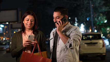 portrait of a couple in the city shopping at night and using smartphone