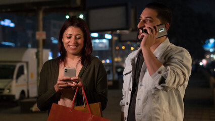 portrait of a couple in the city shopping at night and using smartphone