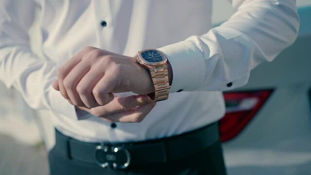 A man wearing an elegant white shirt closes the gold watch on his arm. Close-up visado slow motion shot.