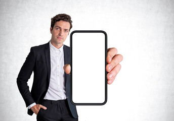 Serious businessman wearing formal wear standing holding smartphone with mockup