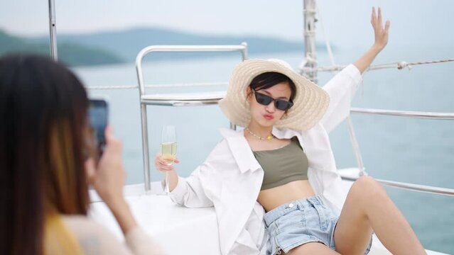 Attractive Asian woman friends enjoy and fun outdoor lifestyle using mobile phone photography together while travel on luxury private catamaran boat yacht sailing in the ocean on summer vacation.