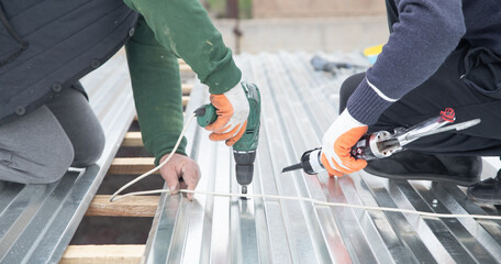 Man installing metal sheet roof by electrical drilling machine. - obrazy, fototapety, plakaty