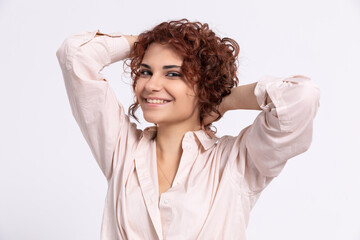 Smiling girl corrects her curly hair with two hands. European.