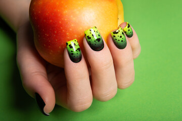 Female neat hand with short natural nails painted with green nail polish holding apple. 