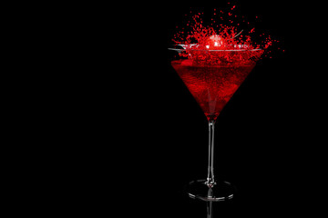 Cherry falling into splashing cocktail in martini glass isolated on black.
