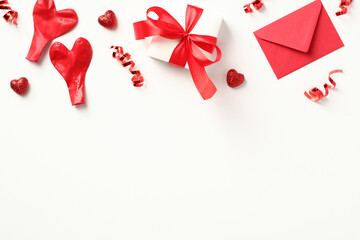 Romantic flat lay composition with love letter envelope, gift box tied with a red ribbon bow, party streamers, and balloons on a white background. Perfect for Valentine's Day or any love concept
