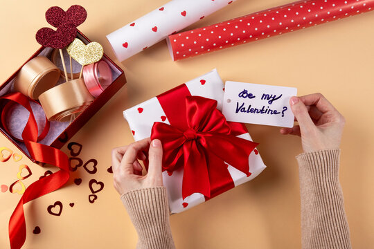 Be My Valentine? Young Woman Packing Gift For Her Boyfriend. Close Up Of Female Hands Packing Gift For Boyfriend. Preparing For The Valentine's Day.