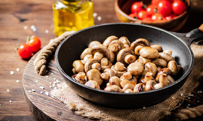 Frying pan with fried mushrooms on a wooden tray. 