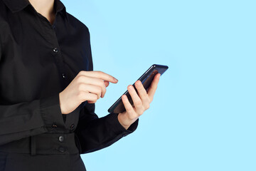 A young teenager girl holds a mobile phone in her hands and dials a number on the screen. Figure isolated on blue background