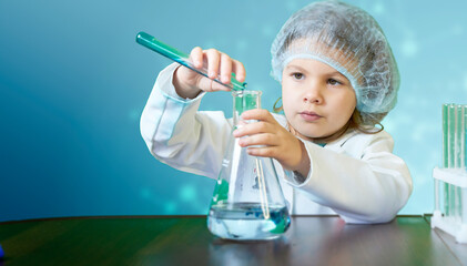 Little kid doing experiments with blue liquid. Cute child wants to become a doctor. Pretty child in white medical robe holds glass flasks with blue liquid on indigo background with hospital symbol.