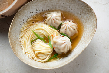 Middle close-up of panasian noodle soup with wontons in a beige bowl, horizontal shot