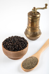 Black pepper grains, ground black pepper and metal mill on a white background