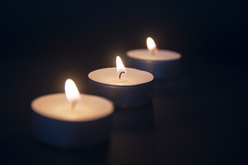 3 tea light candles burning on black background