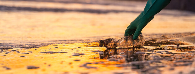 Bottle lying on the seashore. Picked up by a hand with a glove. Reflection of the sunset on the water. Concept recycling, environment