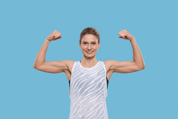 Fototapeta premium Portrait of sportswoman showing muscles on light blue background