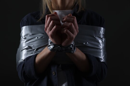 Woman taped up and taken hostage on dark background, closeup