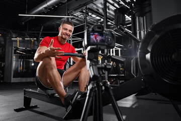 Naklejka na ściany i meble Man recording workout on camera at gym. Online fitness trainer