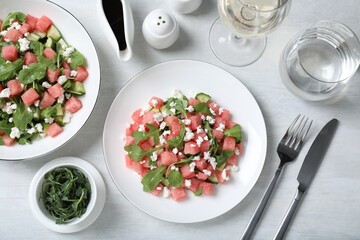 Delicious salad with watermelon, cucumber, arugula and feta cheese served on white wooden table, flat lay