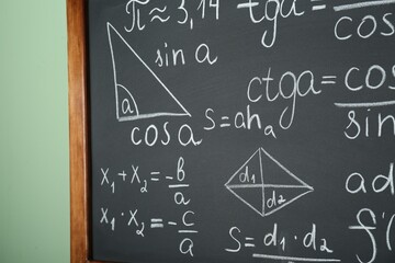 Chalkboard with many different math formulas on green wall, closeup