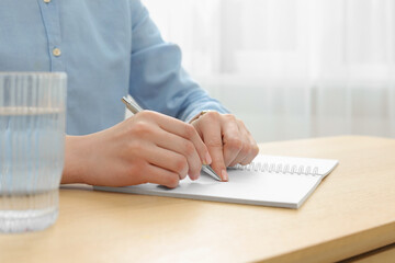 Woman writing in notebook at wooden table, closeup