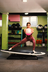 Young woman exercise with a ball on a surfboard in the gym