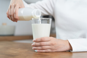 Close-up hands of Person pouring milk into a glass on the table