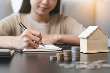 Close up hands of Woman putting coin into piggy bank house model  saving for buy property