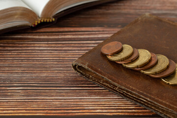 Holy bible book, stack of coin money, and old wallet on wooden table. Copy space. Christian giving, religious offering, and tithing concept.