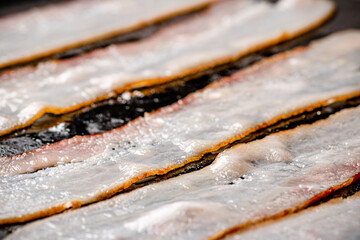 Pieces of bacon are fried in boiling oil with air bubbles. 