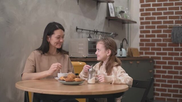 Mother and daughter drink tea in the kitchen and smile. High quality video Full HD video