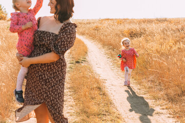 Fototapeta premium Mom with twins, holding a baby in her arms. The girl smiles and walks along the road