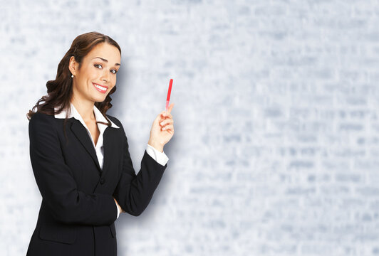 Portrait image of beautiful young business woman in confident suit, showing pointing advertising, white bricks wall background. Businesswoman, executive office worker, teacher gesturing