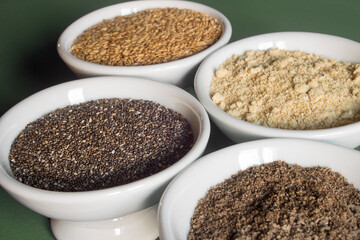 Group of whole and powdered flax and chia seeds on white ceramic bowls. Healthy food and diet.