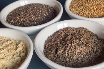 Close-up of a bowl with chia seeds powder along with other bowls of whole and powdered chia and flax seeds. Food and healthy diet.