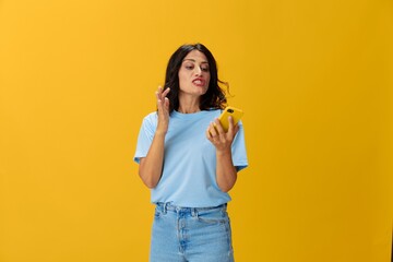 Woman blogger with a phone in her hands in a blue t-shirt and jeans on a yellow background smile signs gestures symbols, online communication and video call, copy space, free background