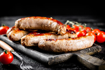 Grilled sausages on a cutting board with tomatoes. 